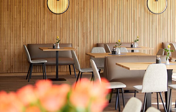 Moderner Gastraum mit Holzwand, runden Wanduhren, gedeckten Tischen und bequemen Stühlen, dekoriert mit kleinen Blumenvasen.