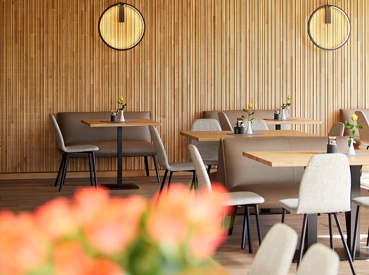 Moderner Gastraum mit Holzwand, runden Wanduhren, gedeckten Tischen und bequemen Stühlen, dekoriert mit kleinen Blumenvasen.