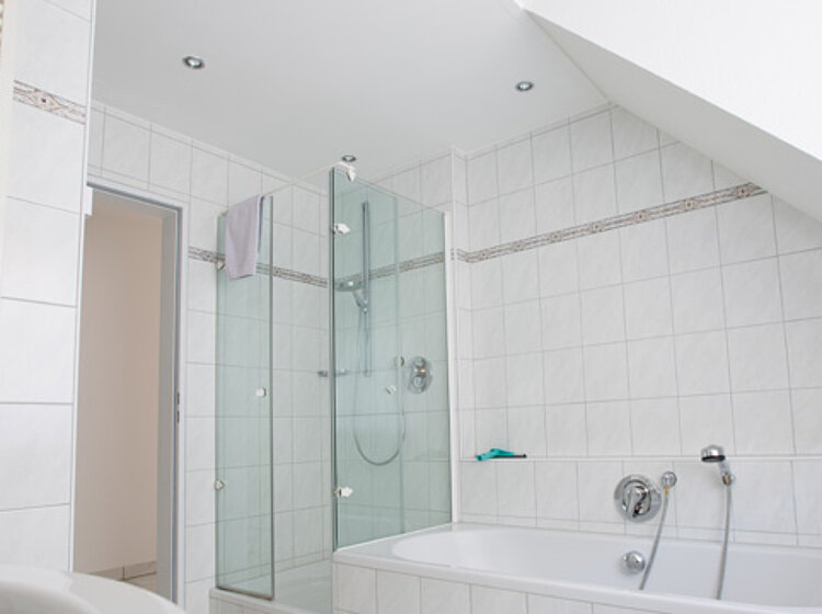 Weiß gefliestes Badezimmer mit Badewanne und angrenzender Glas-Dusche unter einer Dachschräge.