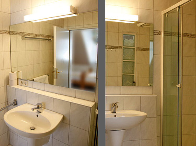 Badezimmer Modernes Badezimmer mit zwei weißen Waschbecken, großen Spiegeln und einer Glasdusche, hell gefliest mit warmem Licht über den Spiegeln.