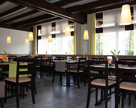 Restaurant mit dunklen Holztischen Blick in ein helles, modernes Restaurant mit dunklen Holztischen und Stühlen, dekoriert mit kleinen Vasen und gelben Tulpen, großen Fenstern und warmen Hängeleuchten.